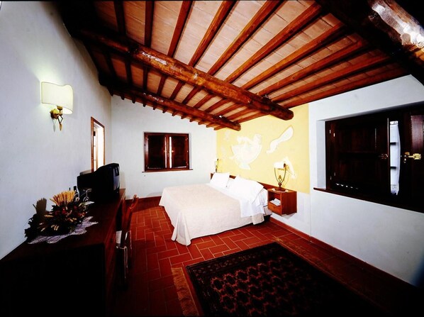 A bedroom with a wooden ceiling, a bed, a nightstand, a lamp, a window, and a wall with a decorative design.