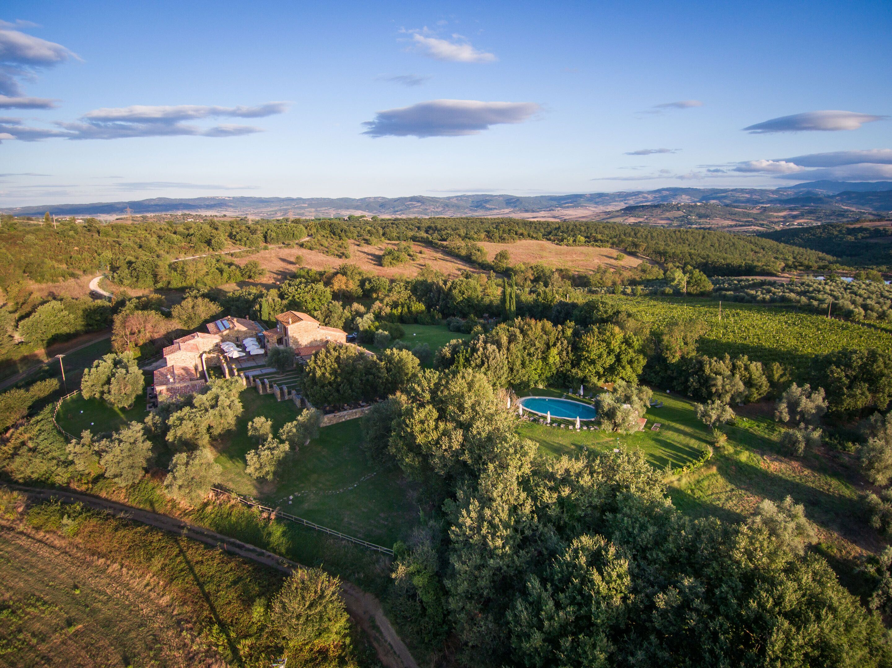 Une vue aérienne d’une propriété comprenant une grande maison entourée d’une végétation luxuriante, une piscine et un chemin sinueux.