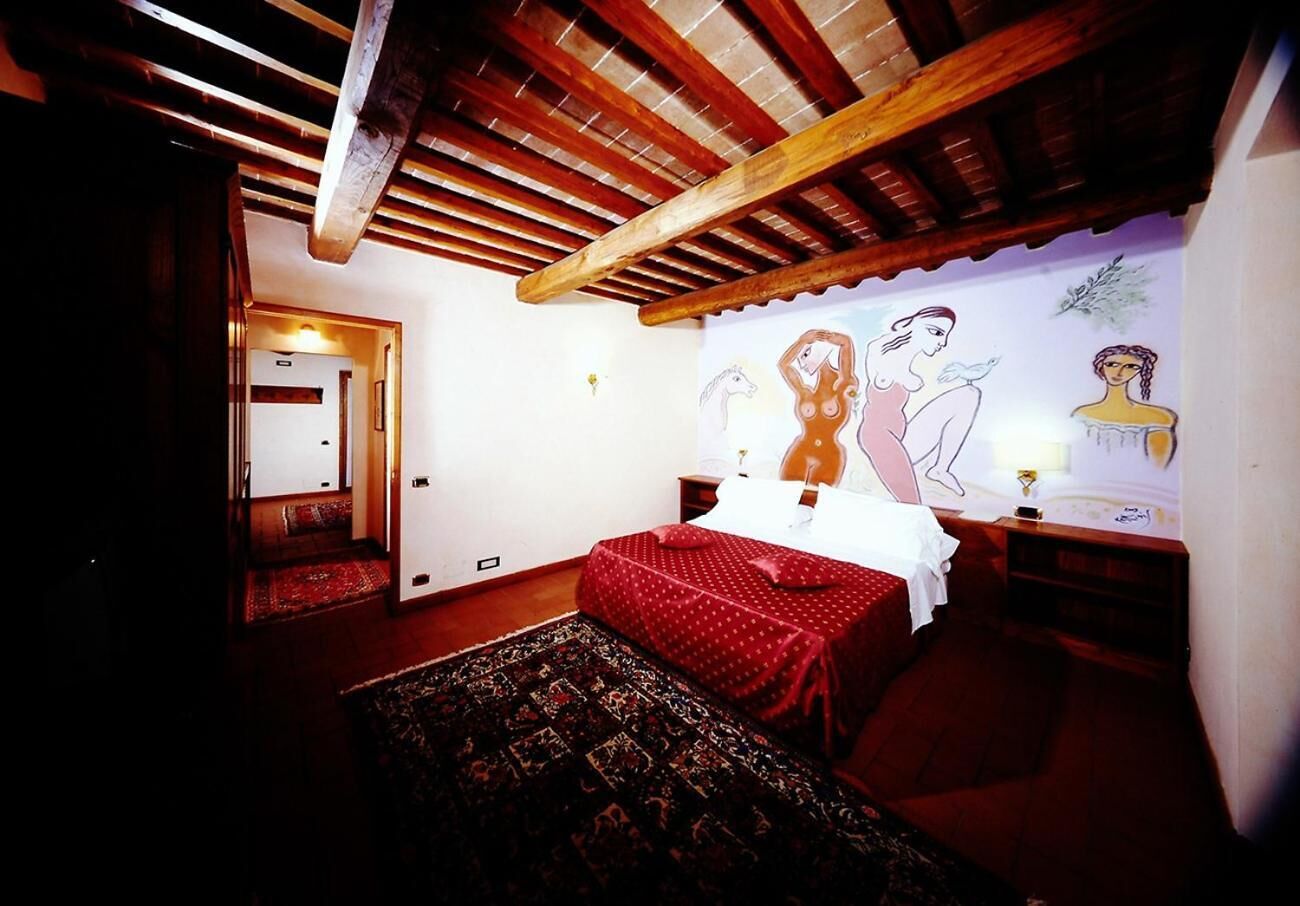 Un dormitorio con techo de madera, una cama con colcha roja de lunares, un tapete estampado y una pared con un mural.