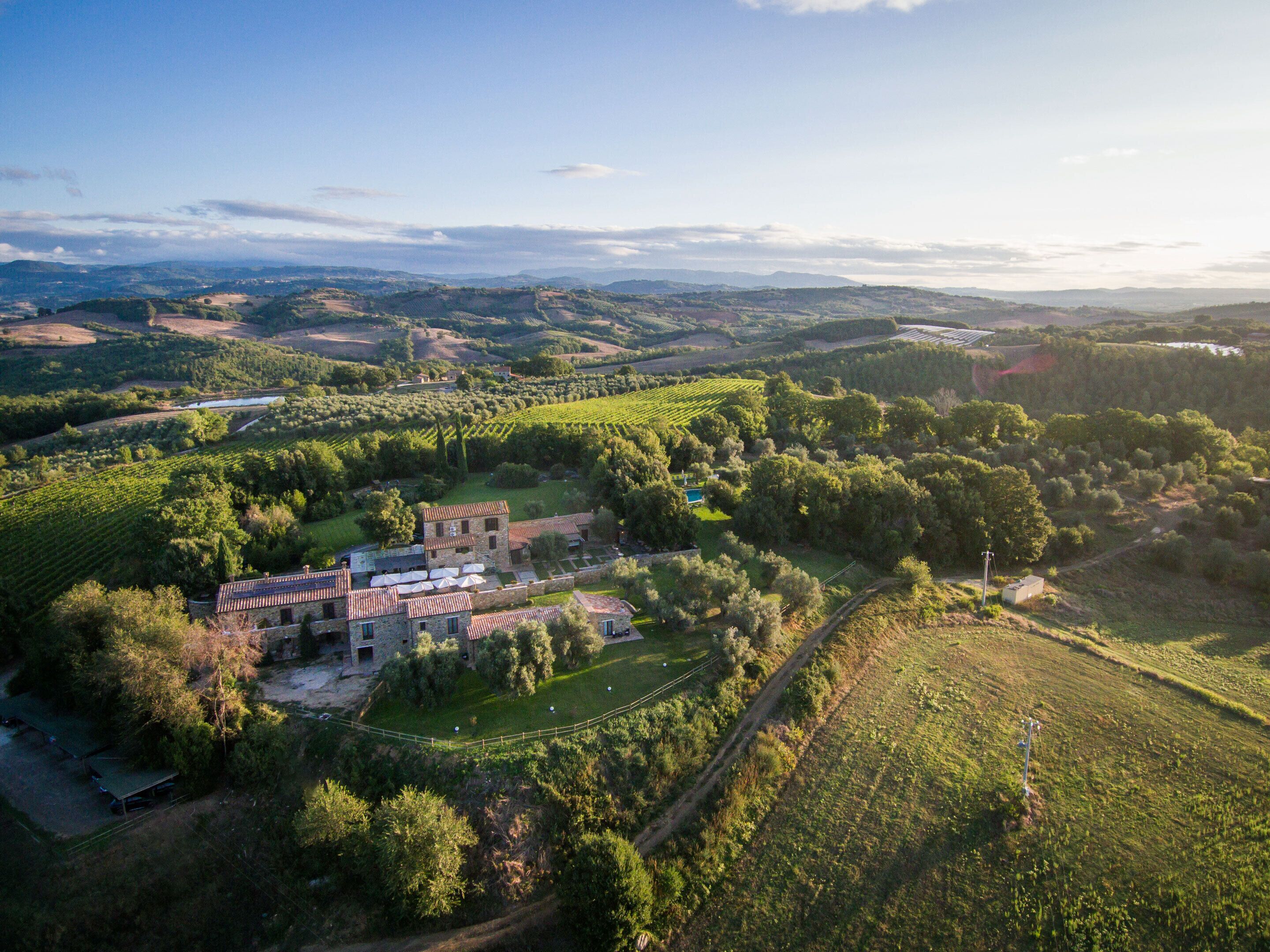 Vista aérea de una finca rural con un amplio edificio de piedra rodeada de viñedos, una piscina y un jardín vallado.