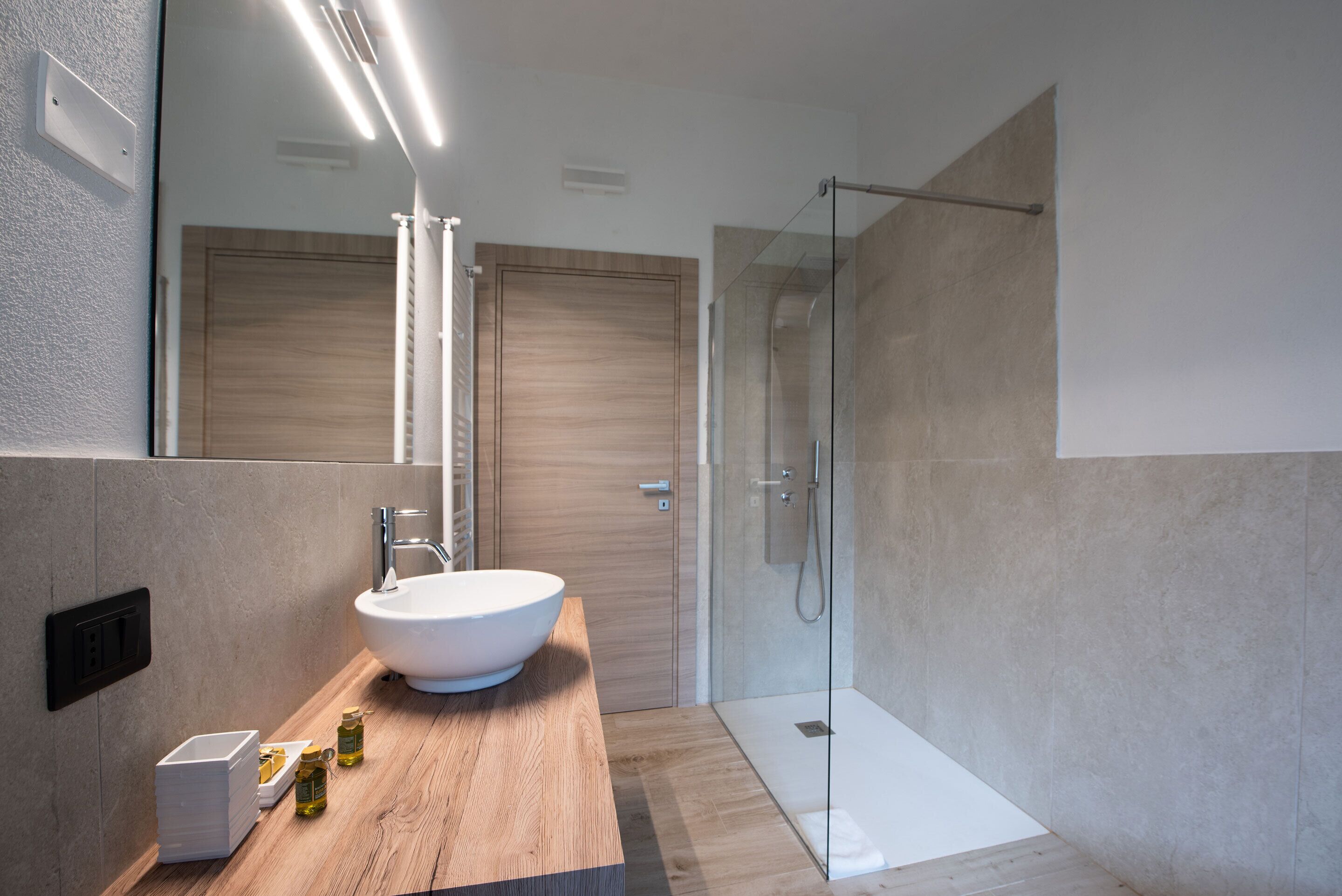 A modern bathroom with a large white sink, wooden countertop, and a glass-enclosed shower.