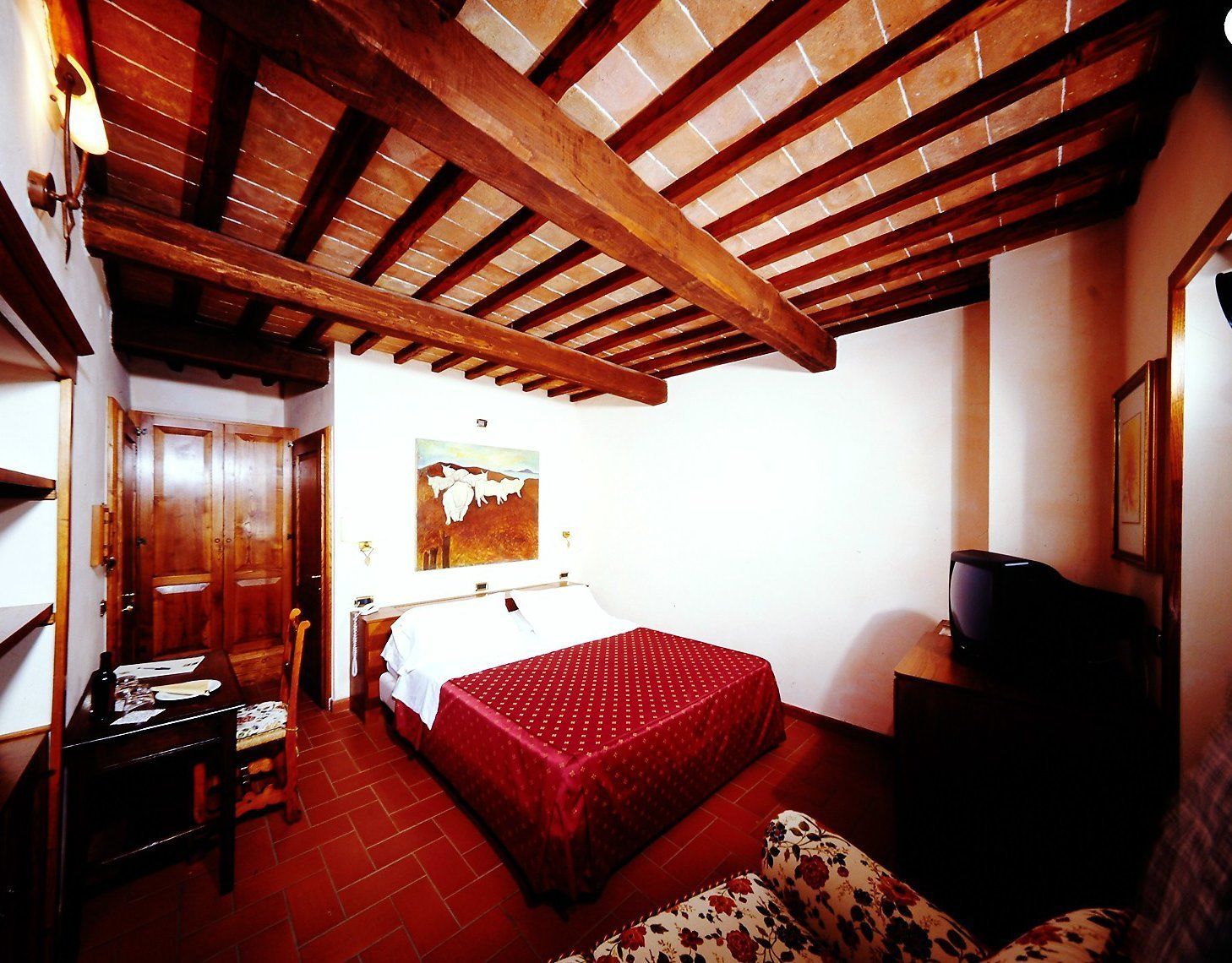 Un dormitorio con techo de madera, una cama con colcha roja, un escritorio de madera y un televisor sobre un mueble de madera.