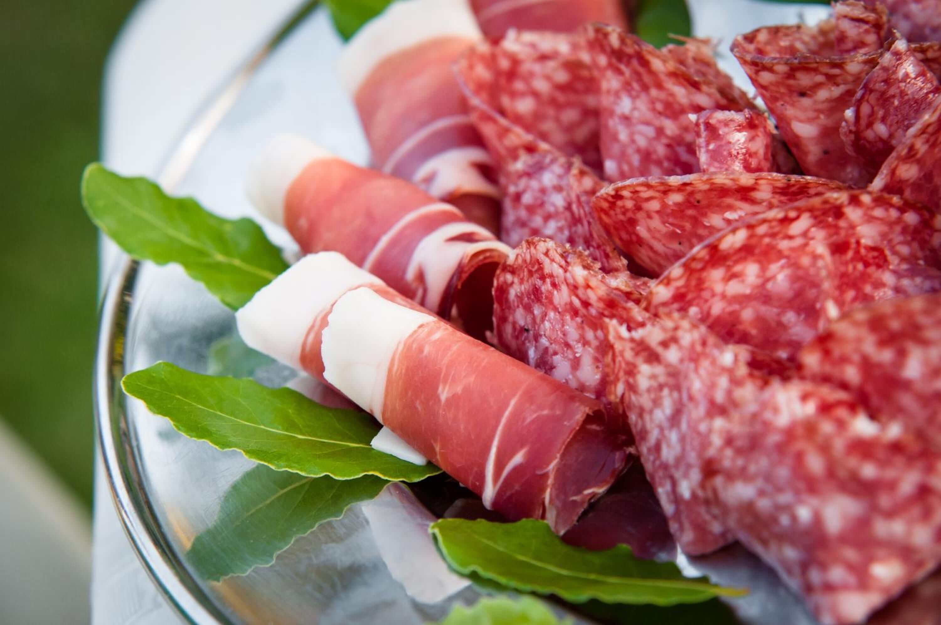 A plate of sliced cured meats with bay leaves.