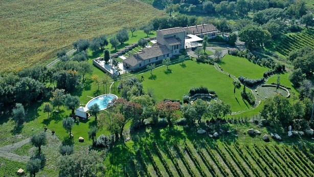 Vista aérea de una propiedad con una casa grande rodeada de campos verdes y una piscina.