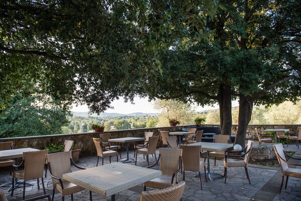 An outdoor patio area with wicker tables and chairs, stone flooring, and potted plants. - Fattoria Pianetti (Manciano)