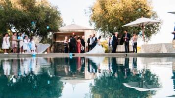 Une piscine dont l’eau reflète les personnes et les arbres, entourée d’un belvédère et de parasols.