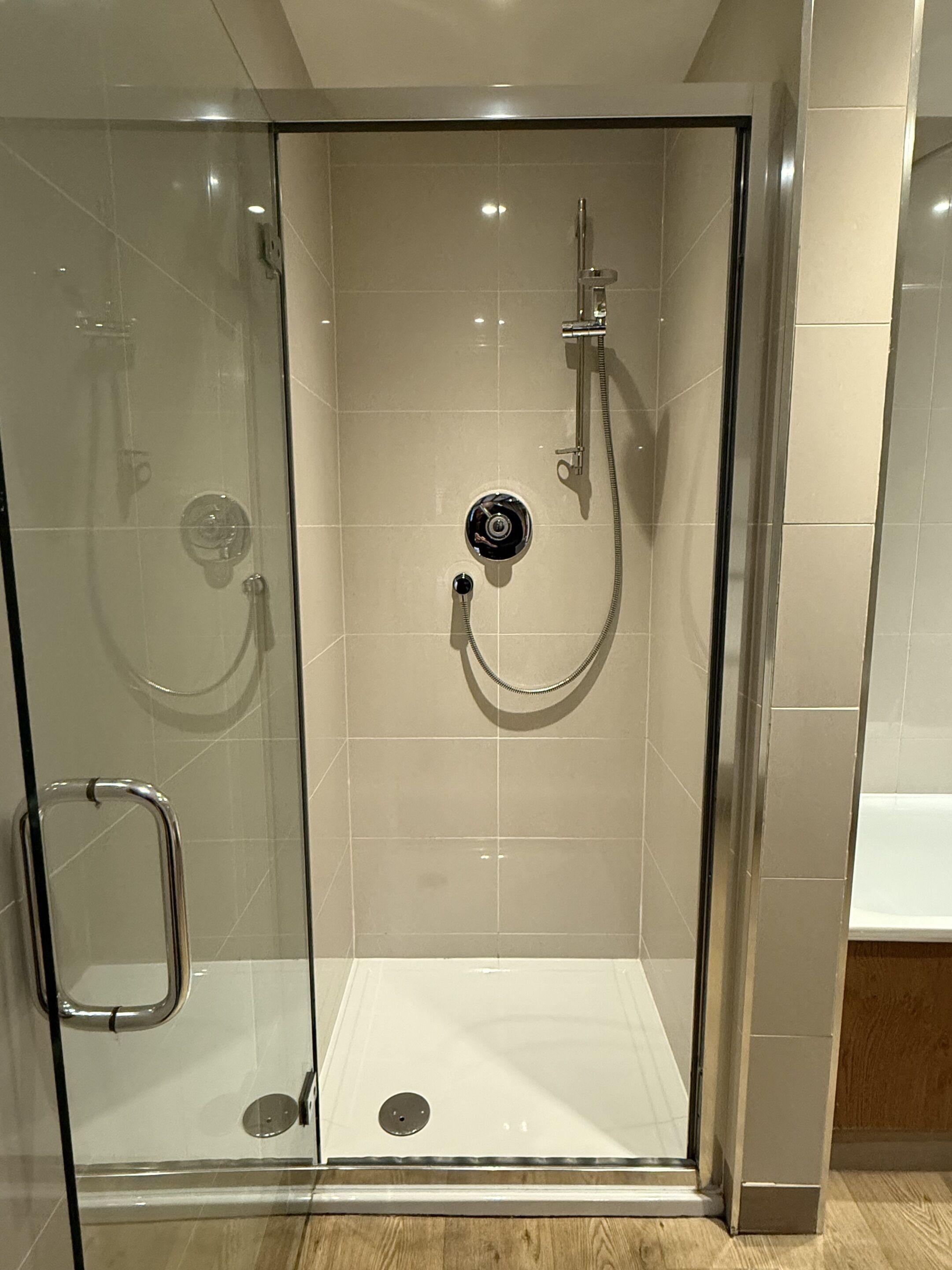 Une cabine de douche fermée par des parois en verre, dotée d’un pommeau de douche à main et d’un robinet fixé au mur.