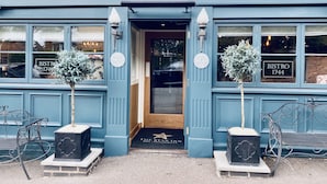 The exterior of Bistro 1744, featuring a blue facade, a wooden door, and two potted plants.