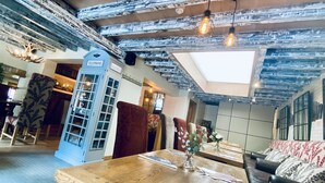 A rustic interior with exposed wooden beams, a wooden dining table, a sofa, and a telephone booth.