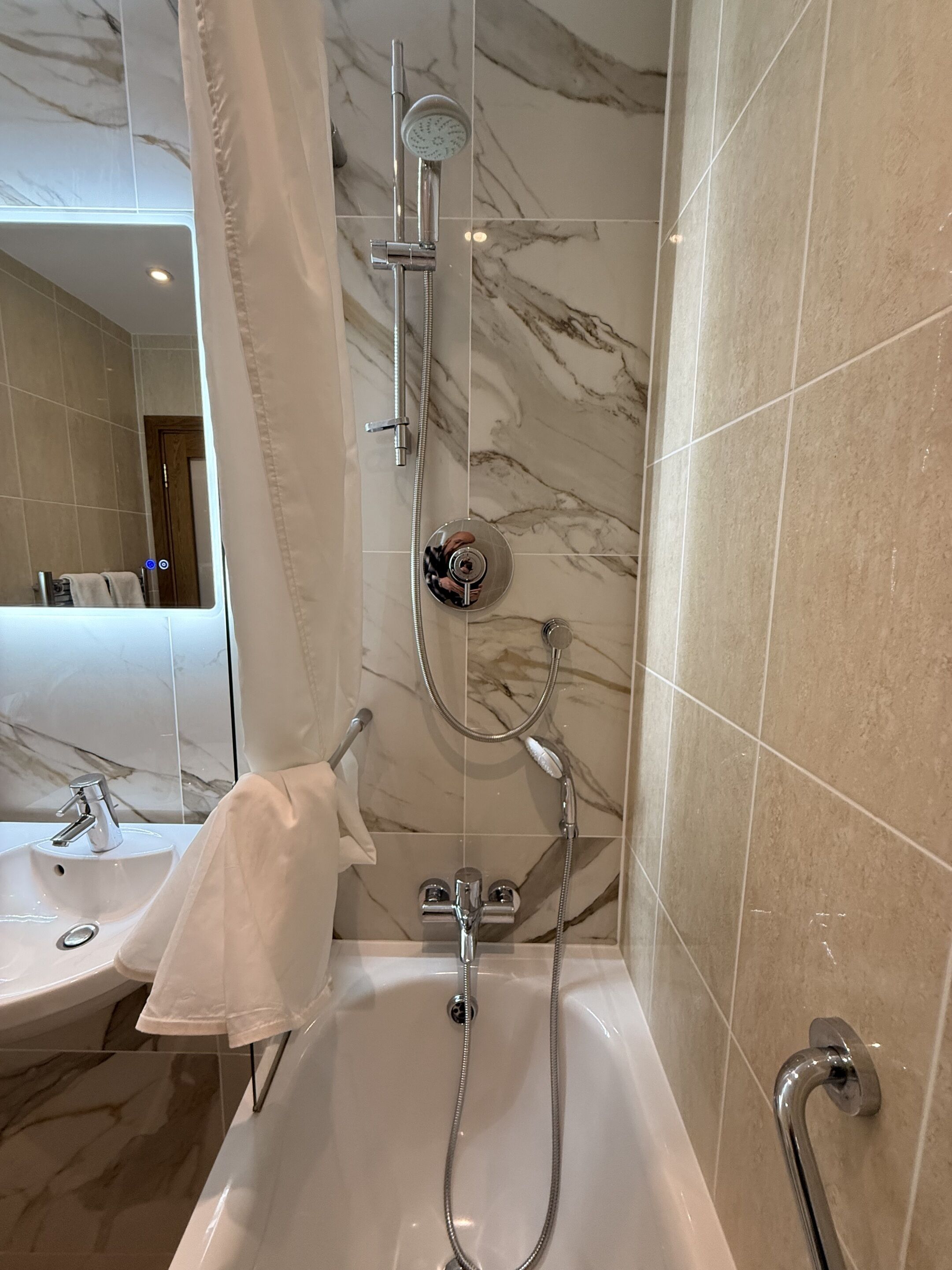 A modern bathroom with a bathtub, shower, and a large mirror.