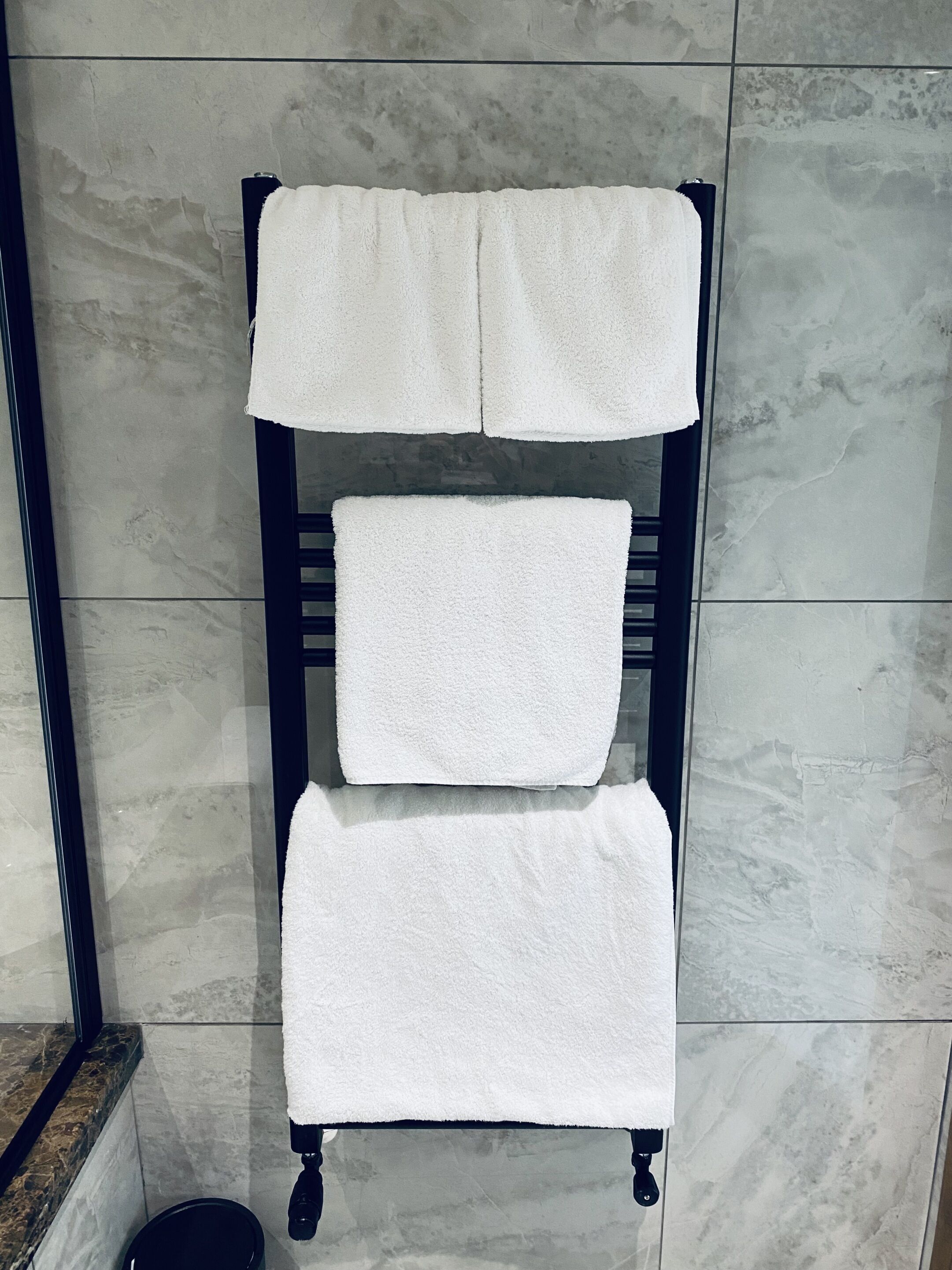 A towel rack with three white towels against a tiled wall.