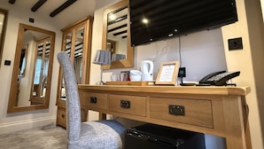 A hotel room with a wooden desk, a chair, a flat-screen TV mounted on the wall, a coffee maker, and a telephone.