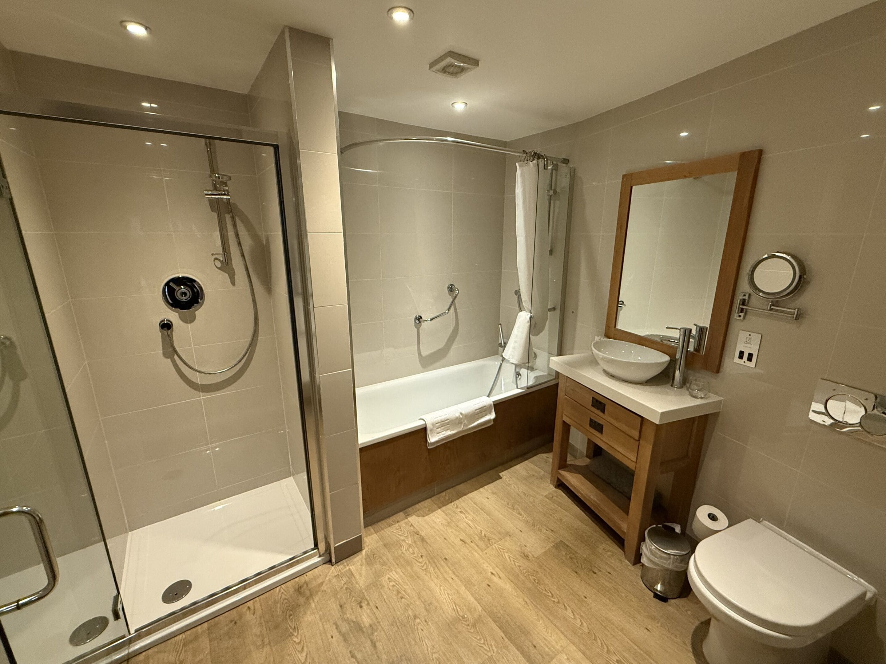 Une salle de bain moderne dotée d’une douche à parois de verre, d’une baignoire sur pieds, d’un meuble-lavabo en bois et de toilettes.