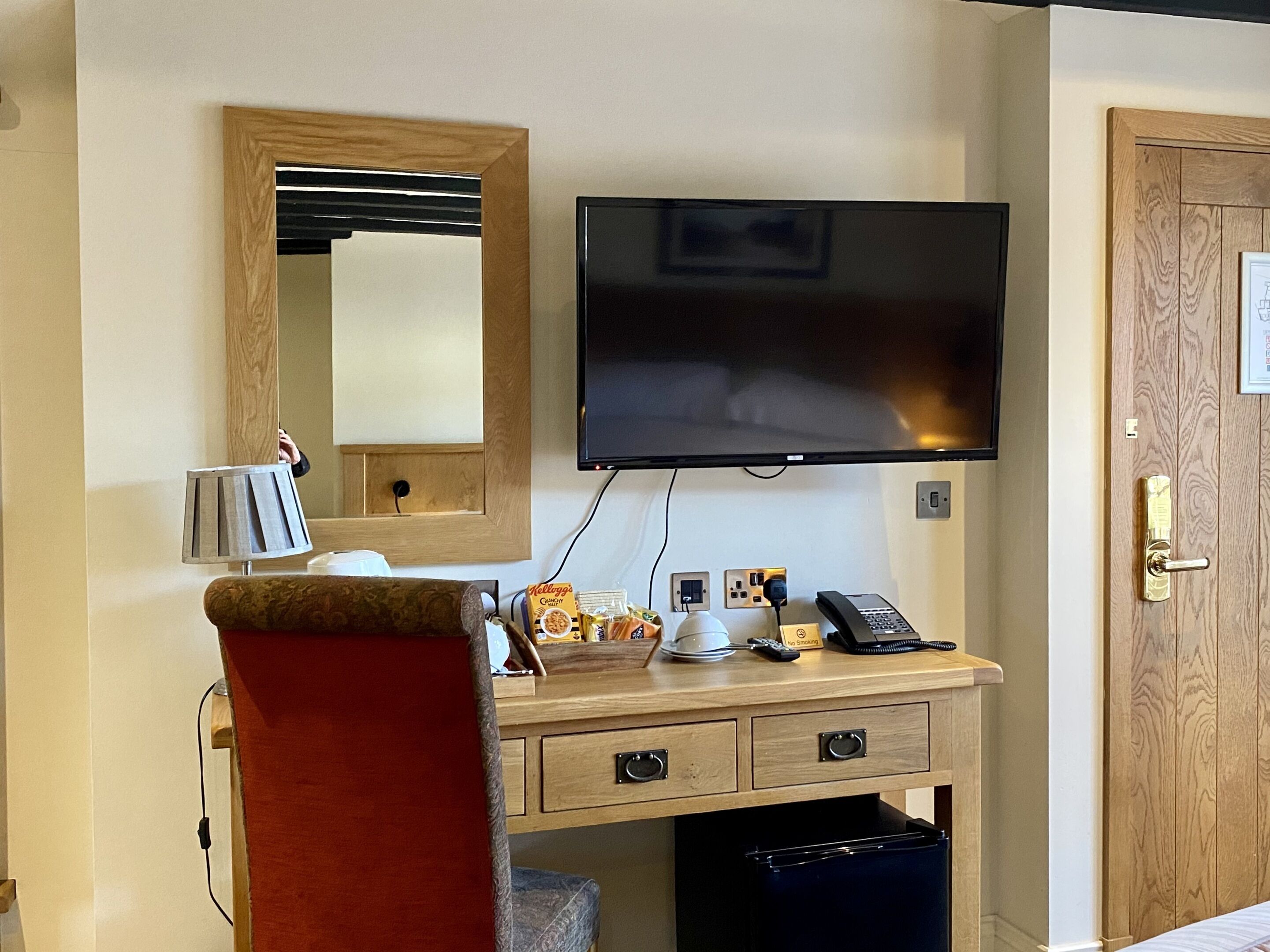 Une chambre d’hôtel avec un bureau en bois, un téléviseur à écran plat fixé au mur, un téléphone et une petite poubelle.