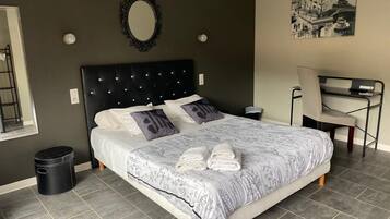 A bedroom with a bed, a desk, a chair, a trash bin, and a wall-mounted mirror.