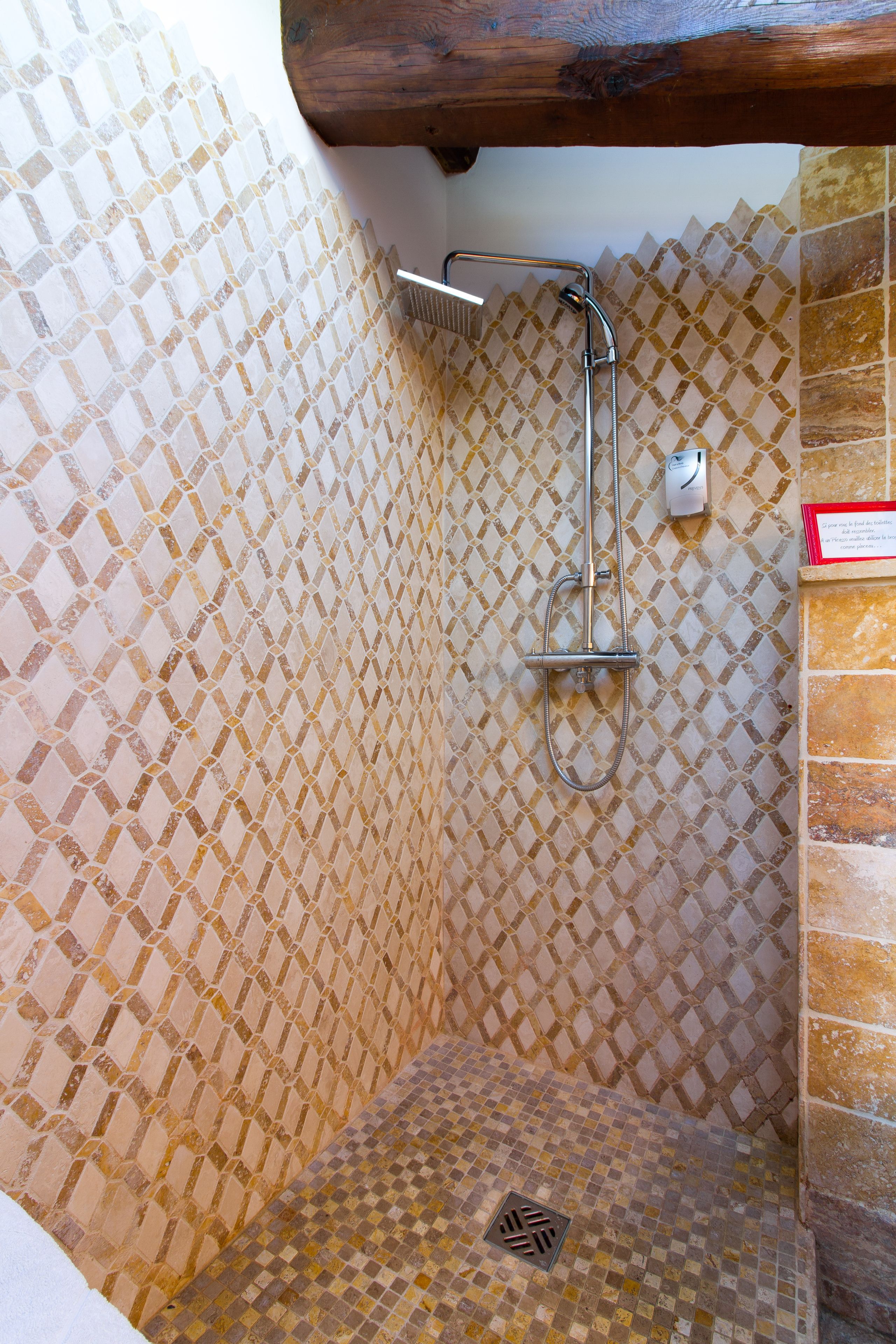 A shower area with a tiled wall and a wooden beam above.