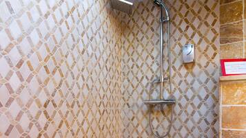 A shower area with a tiled wall and a wooden beam above.