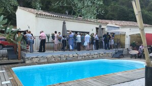 A swimming pool with a wooden deck and stone wall, surrounded by a fence. - Auberge Les Galets Hotel Restaurant (Peyruis)