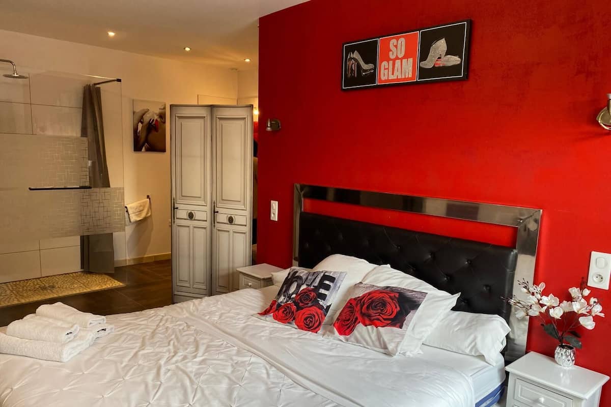 A bedroom with a red accent wall, a black upholstered headboard, white bedding, and a nightstand with a vase of flowers.