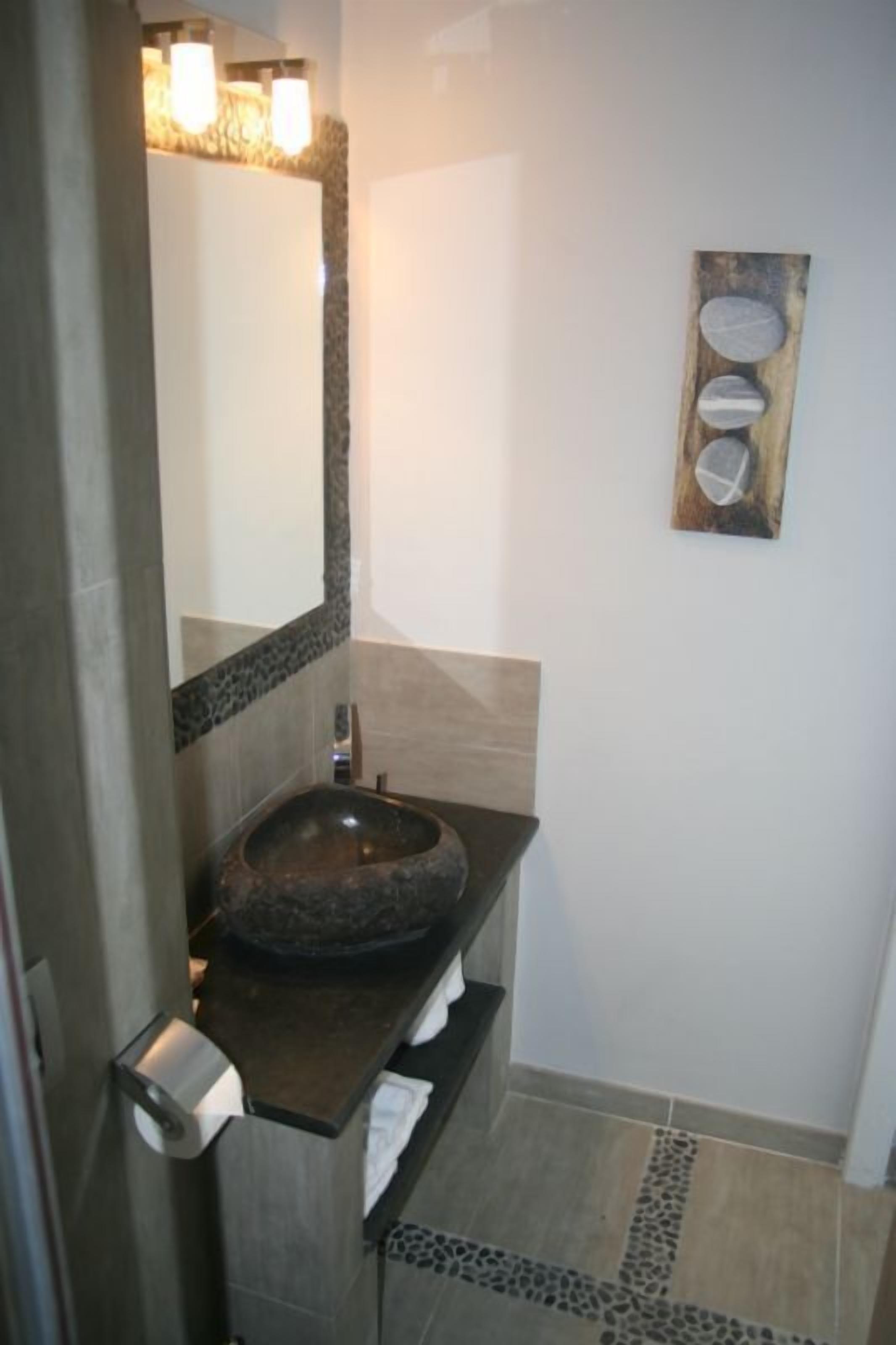 Un baño con un lavamanos de piedra, un espejo y una obra de arte de madera en la pared.