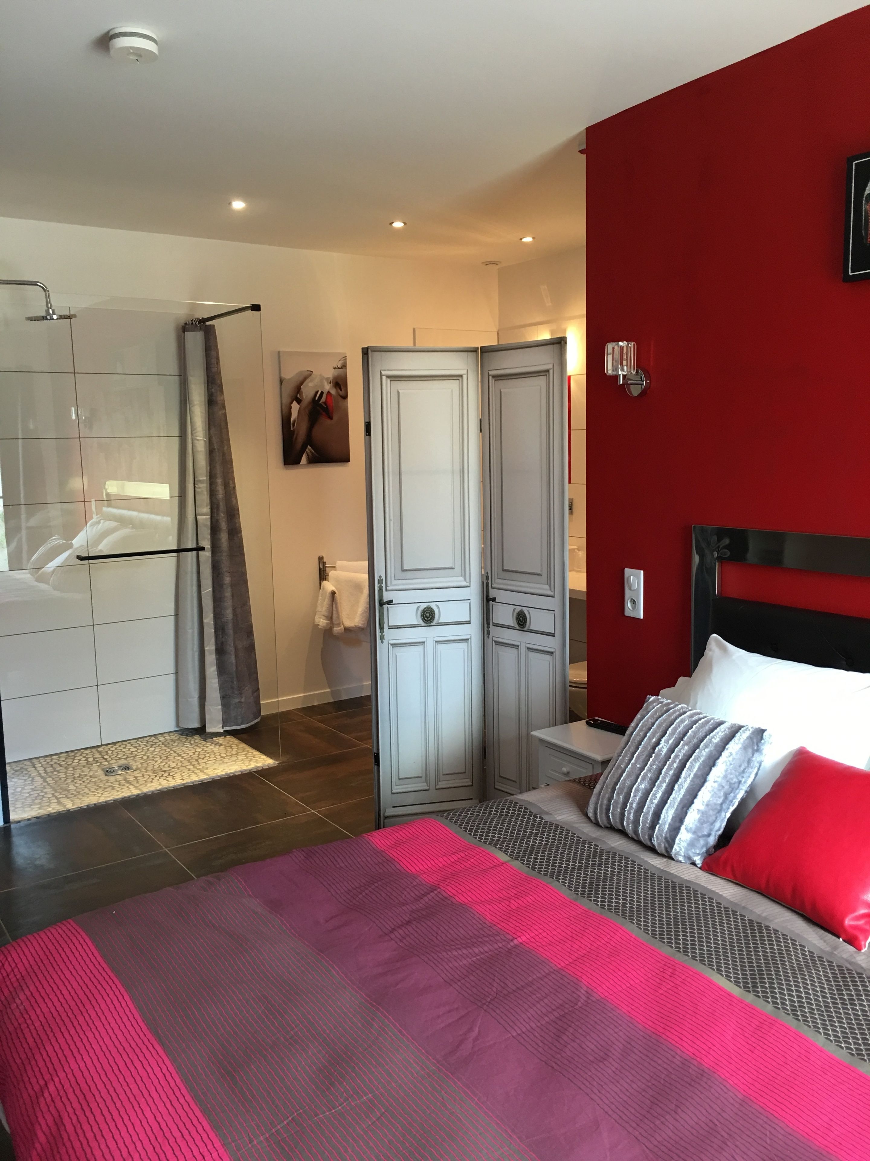 A modern bedroom with a large bed, a shower area, and a red accent wall.