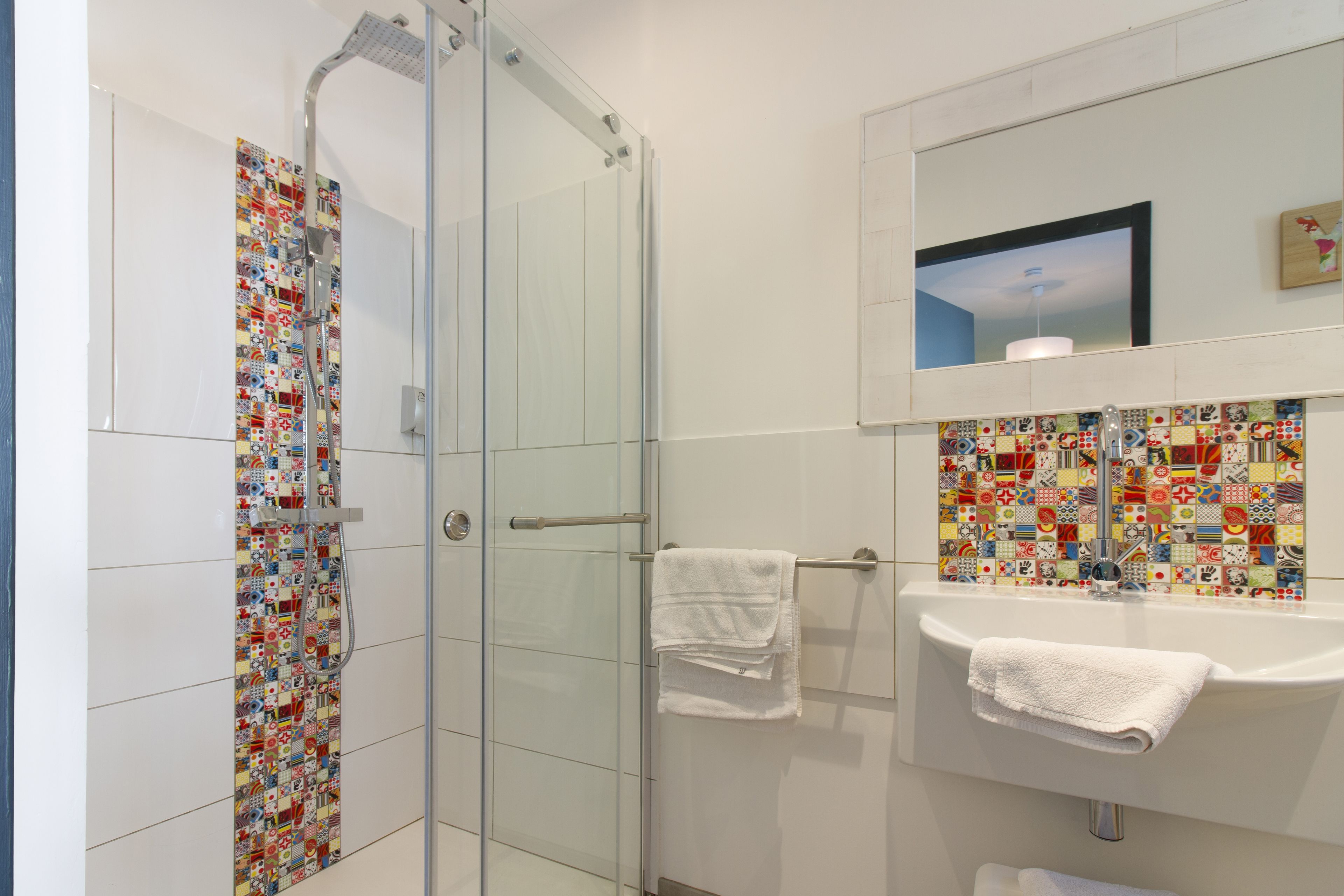 A bathroom with a glass shower enclosure, a sink with a mirror, and a tiled backsplash.