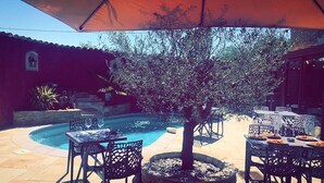 An outdoor patio with a pool, surrounded by tables and chairs, and a large umbrella providing shade. - Auberge Les Galets Hotel Restaurant (Peyruis)