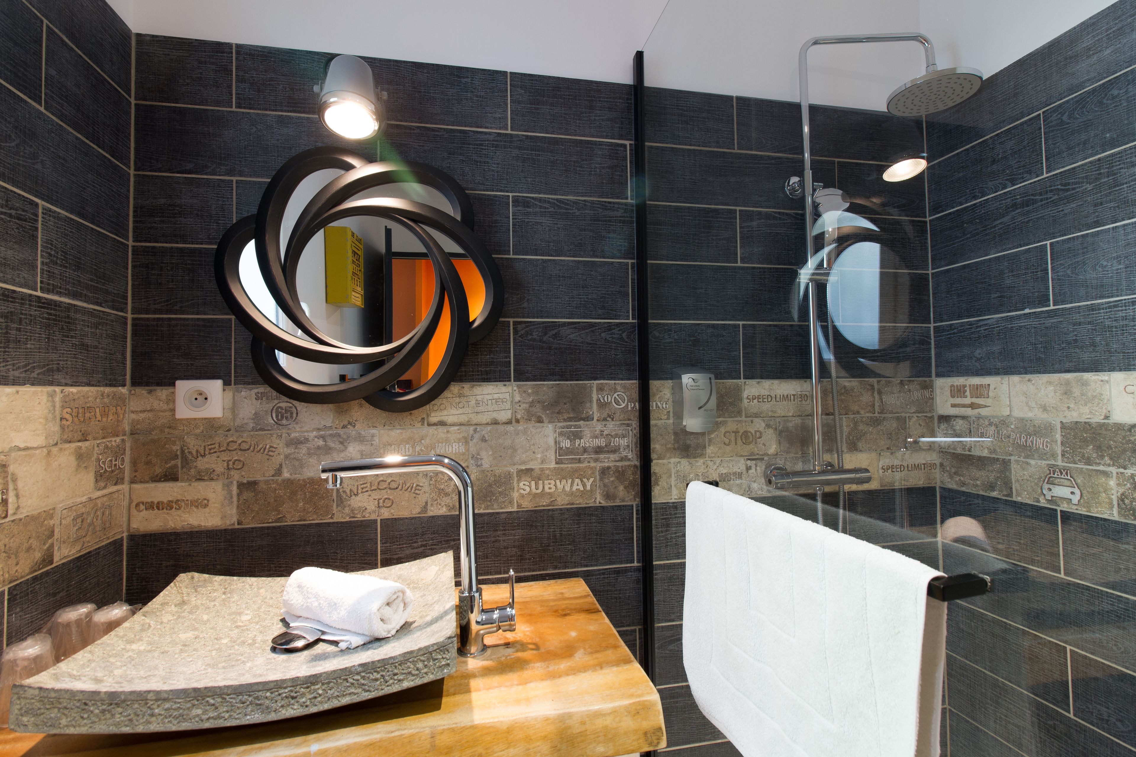 Un baño moderno con un lavabo de piedra, un espejo con marco circular y una ducha con cerramiento de vidrio.