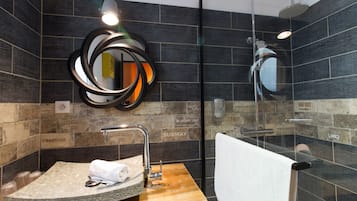 Un baño moderno con un lavabo de piedra, un espejo con marco circular y una ducha con cerramiento de vidrio.