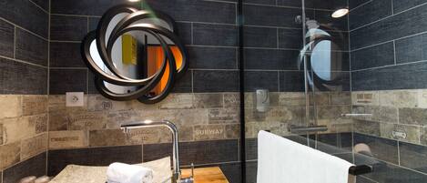 Un baño moderno con un lavabo de piedra, un espejo con marco circular y una ducha con cerramiento de vidrio.