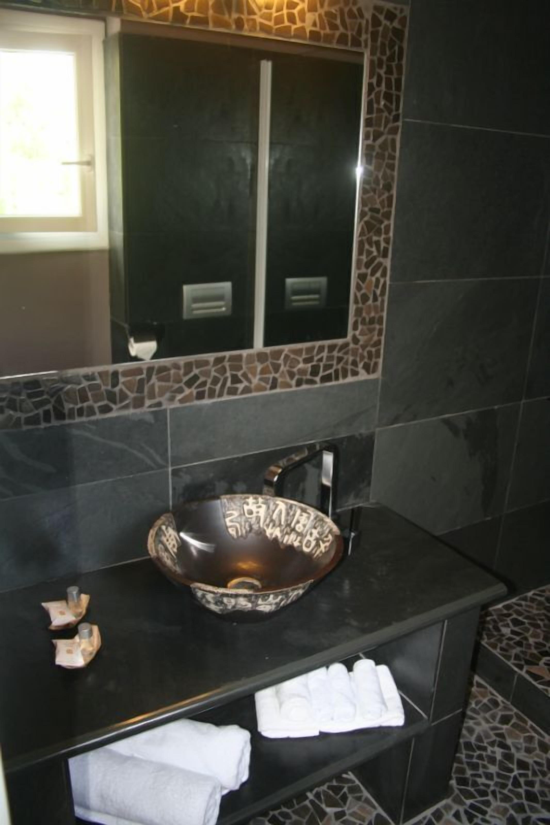 A bathroom with a large, decorative vessel sink, a mirror above it, and a shelf with folded towels.