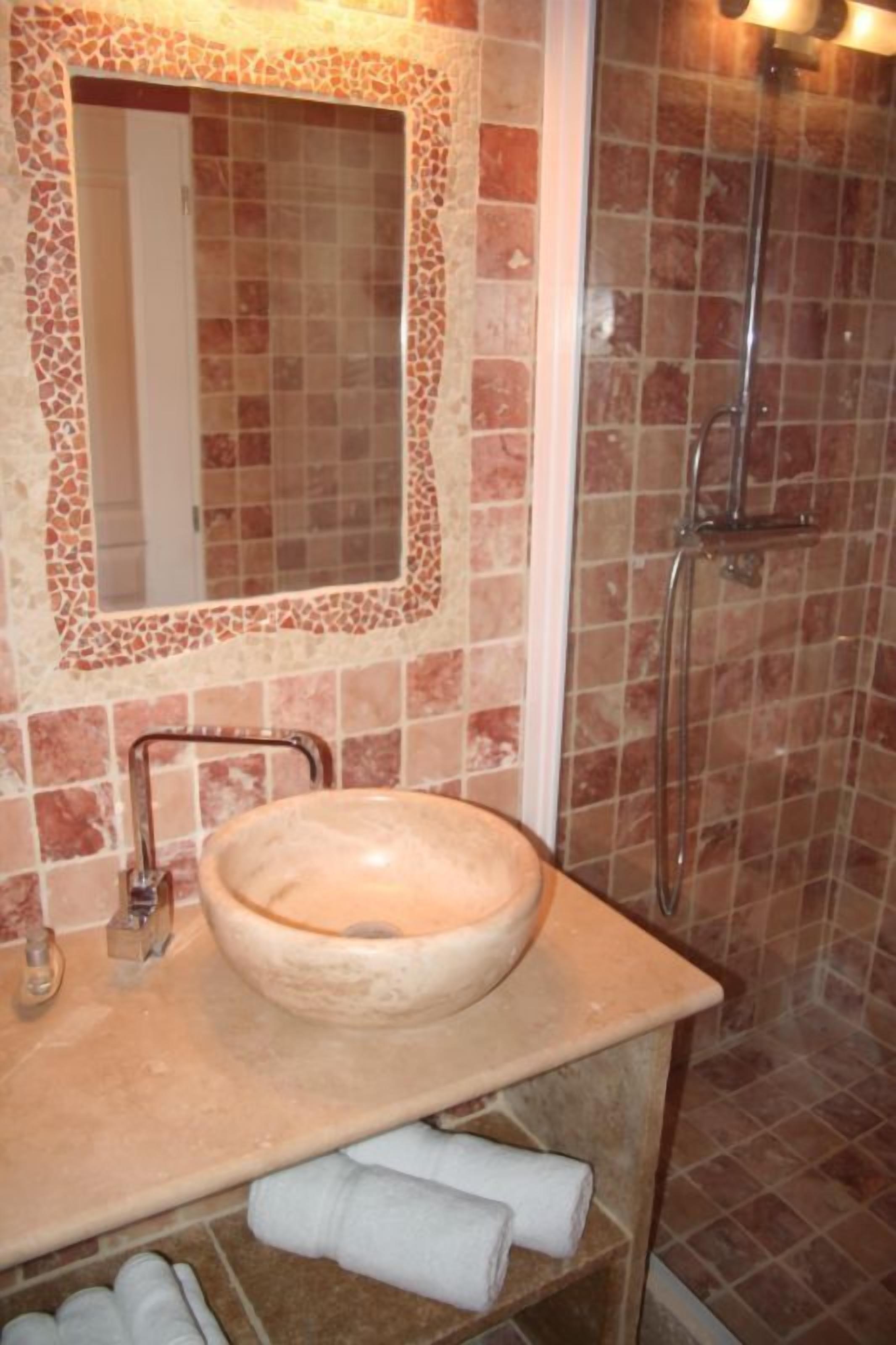 A bathroom with a large, round sink, a mirror with a mosaic frame, and a shower area with tiled walls.