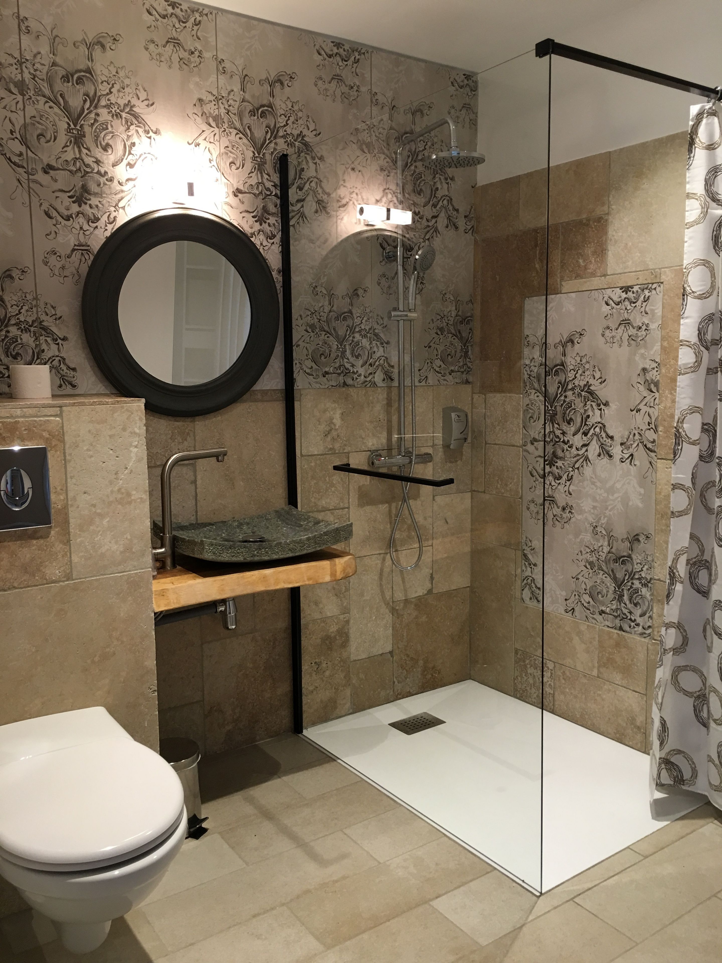 Un baño moderno con cabina de ducha de vidrio, un espejo redondo, un lavamanos con encimera de madera y un inodoro.