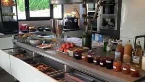 A modern kitchen with a central island stocked with food items, a built-in oven, and a large window providing natural light. - Auberge Les Galets Hotel Restaurant (Peyruis)