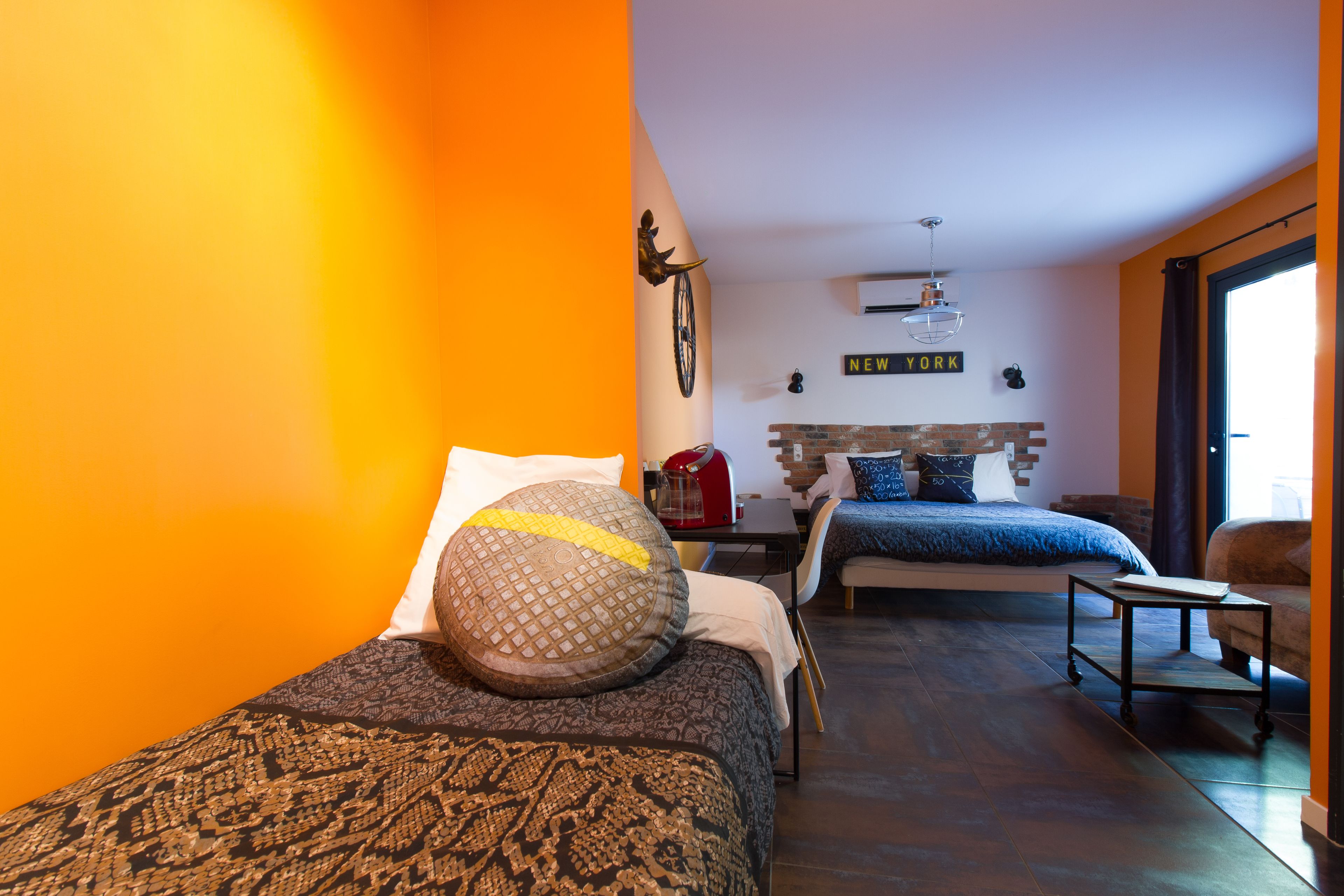 A modern bedroom with two beds, a brick fireplace, and a large window.