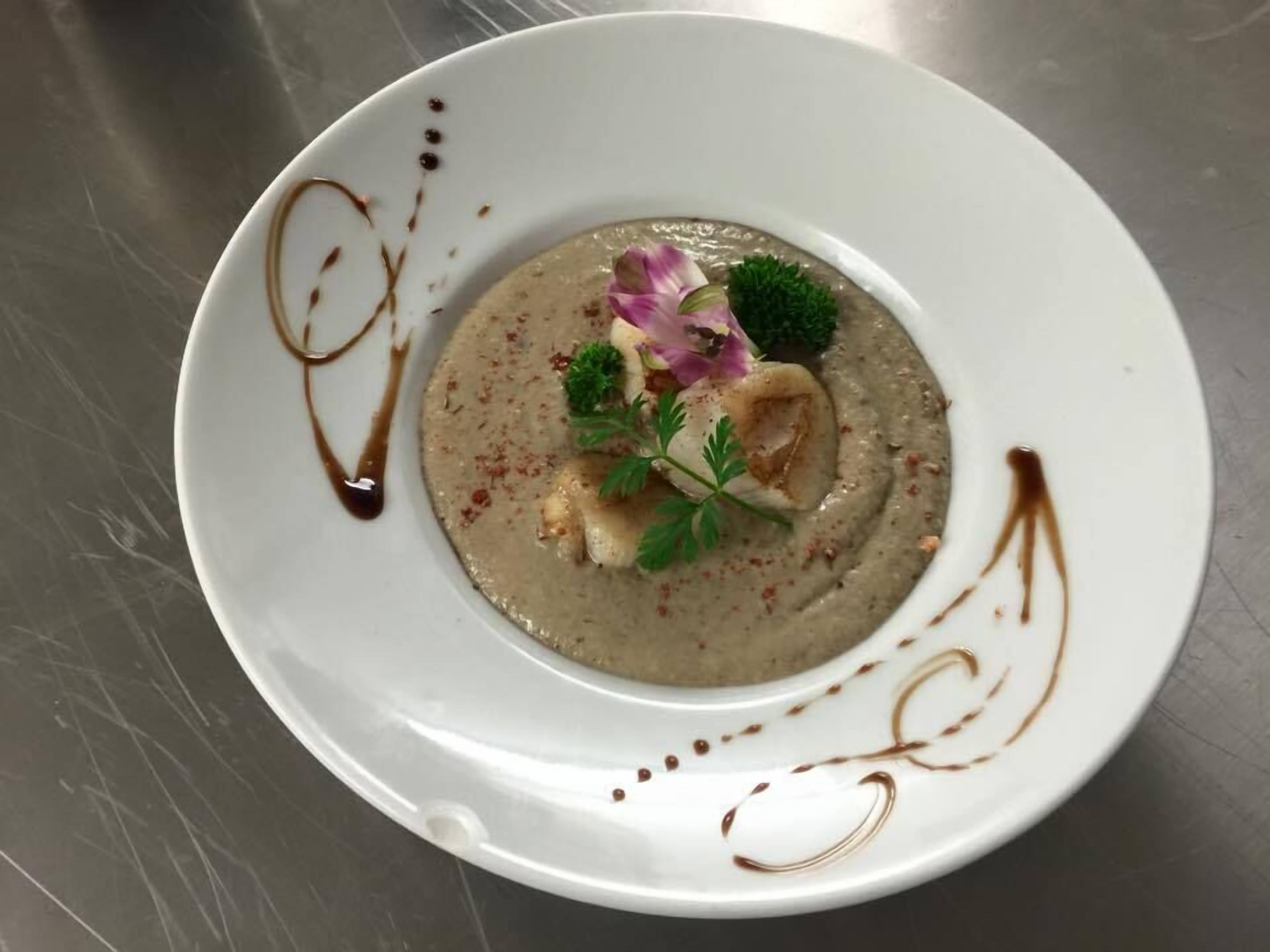 Un plato blanco con crema de sopa, decorado con perejil, una flor y un trozo de carne.