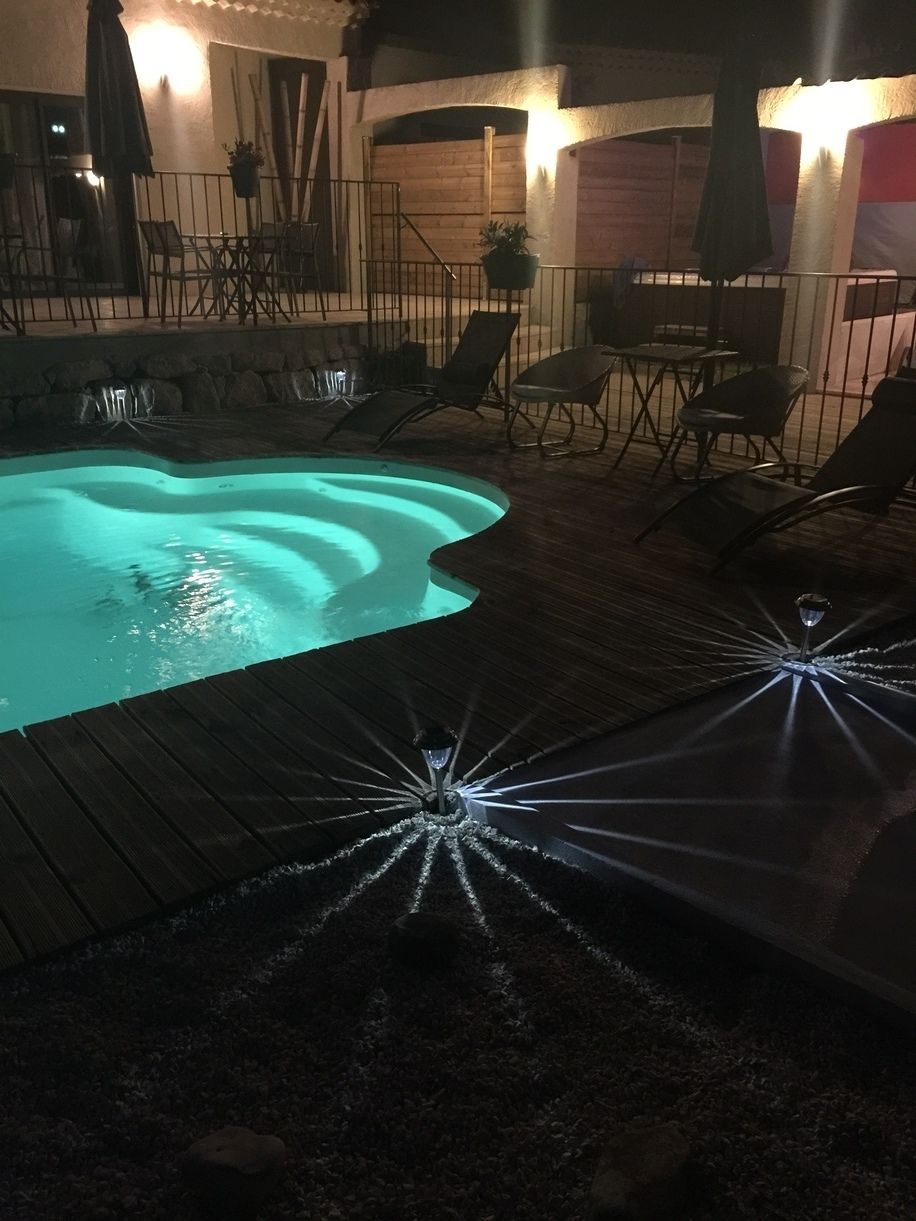 A swimming pool with a wooden deck, surrounded by outdoor furniture and a fence.