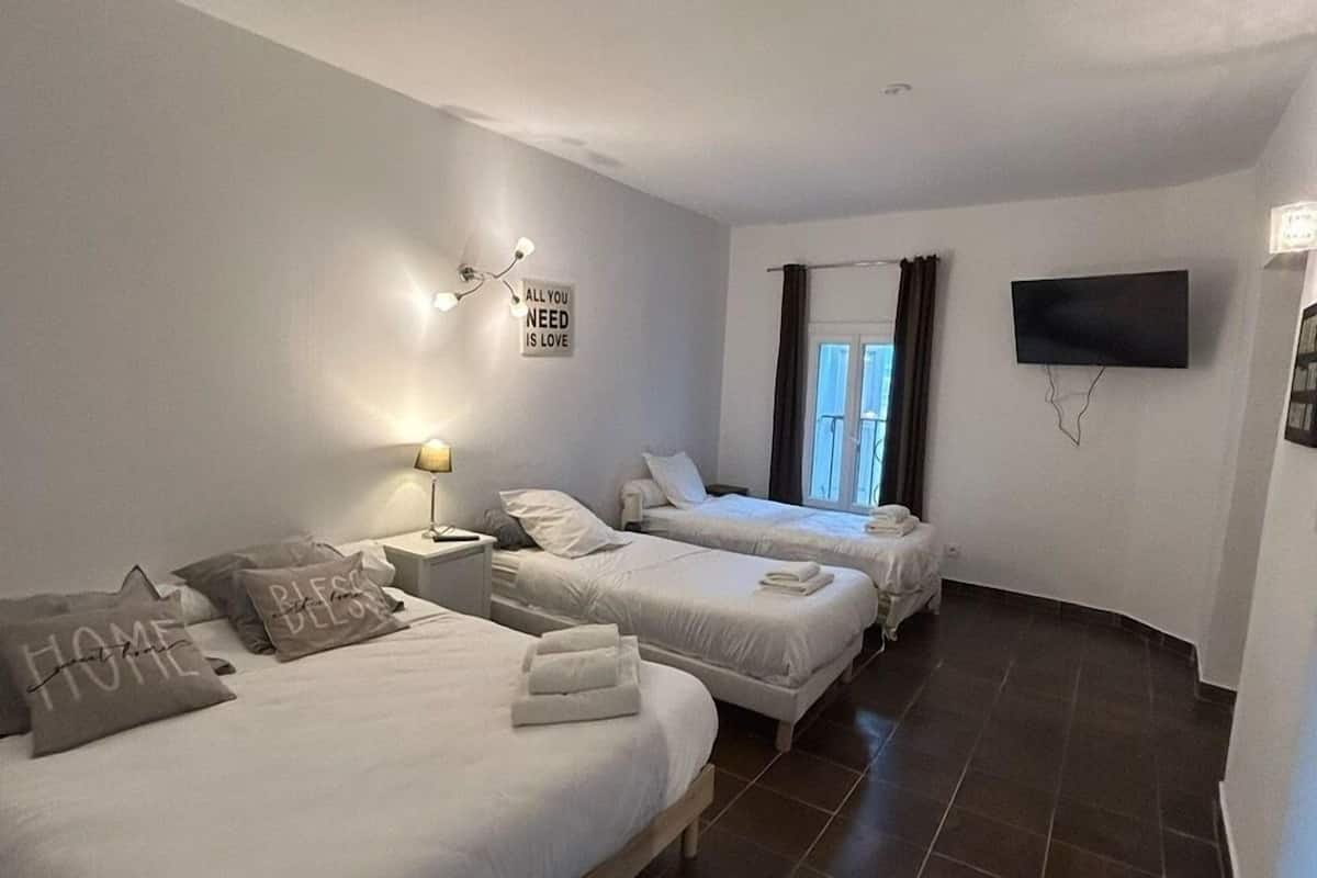 A hotel room with two beds, a flat-screen TV, a wall-mounted light, and a window with curtains.