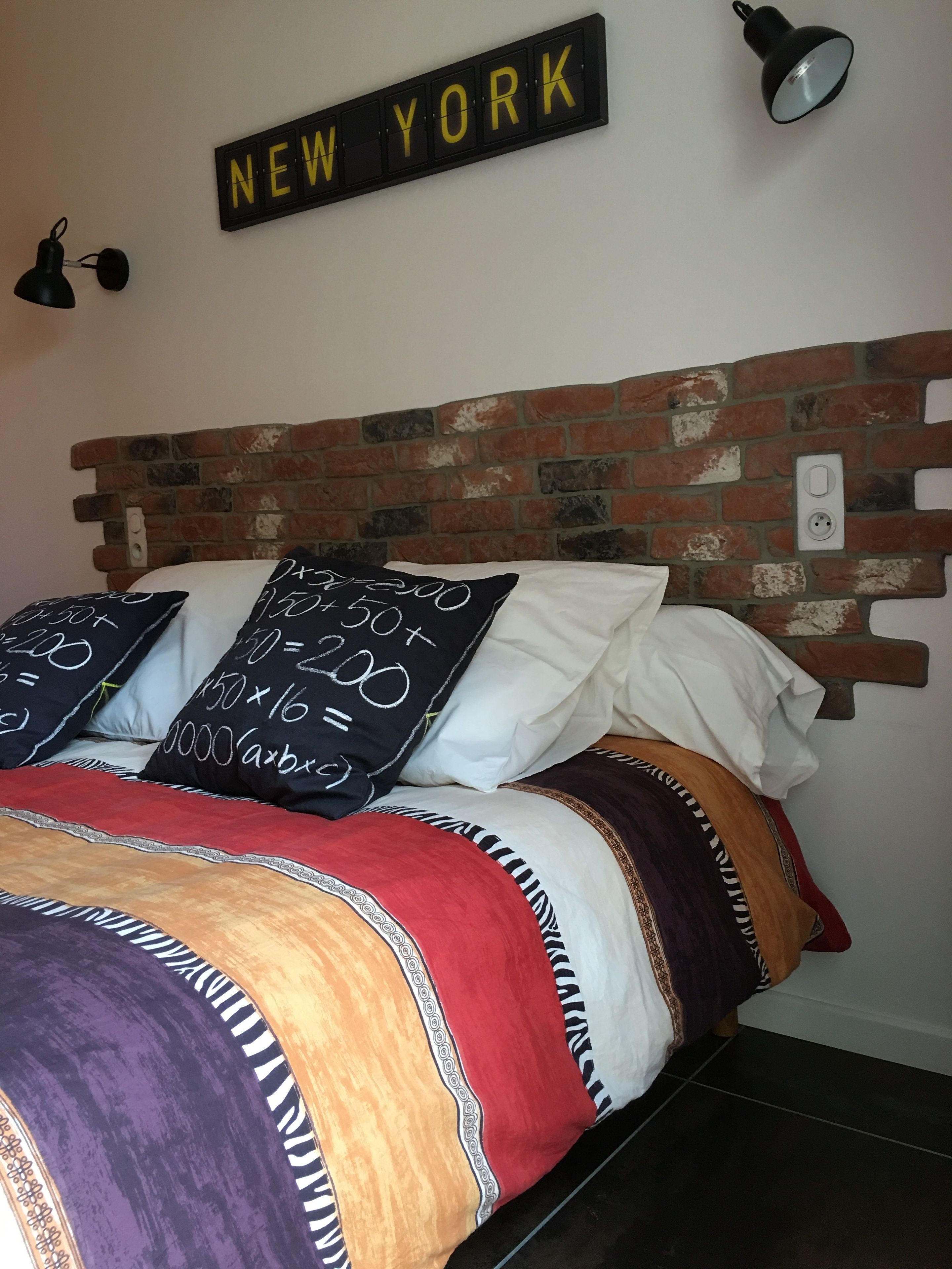 A bed with a brick headboard, multiple pillows with mathematical equations, and a sign that reads "NEW YORK" on the wall.