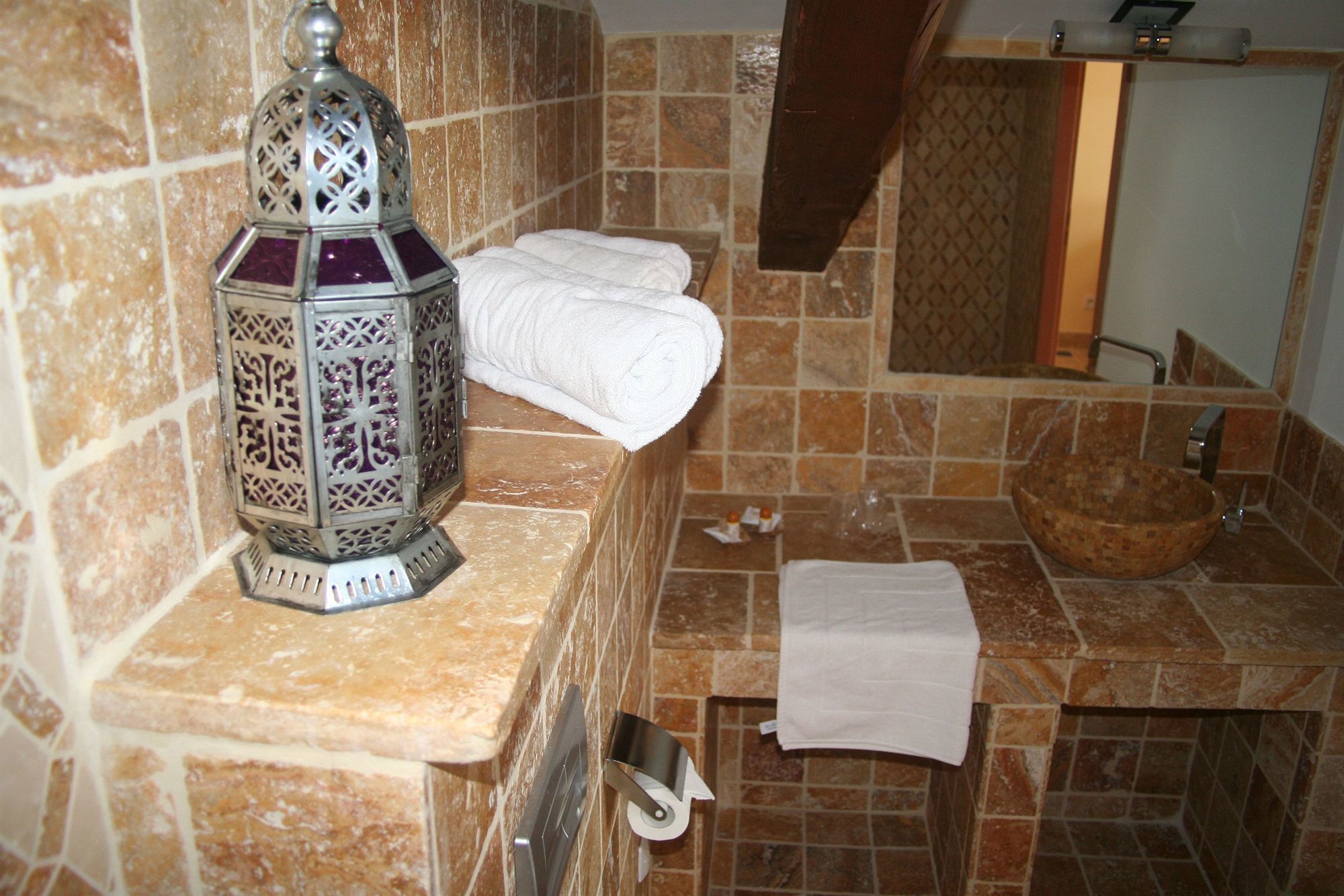 A bathroom with a stone tile backsplash, a decorative metal lantern, a white towel, and a wooden bowl sink.
