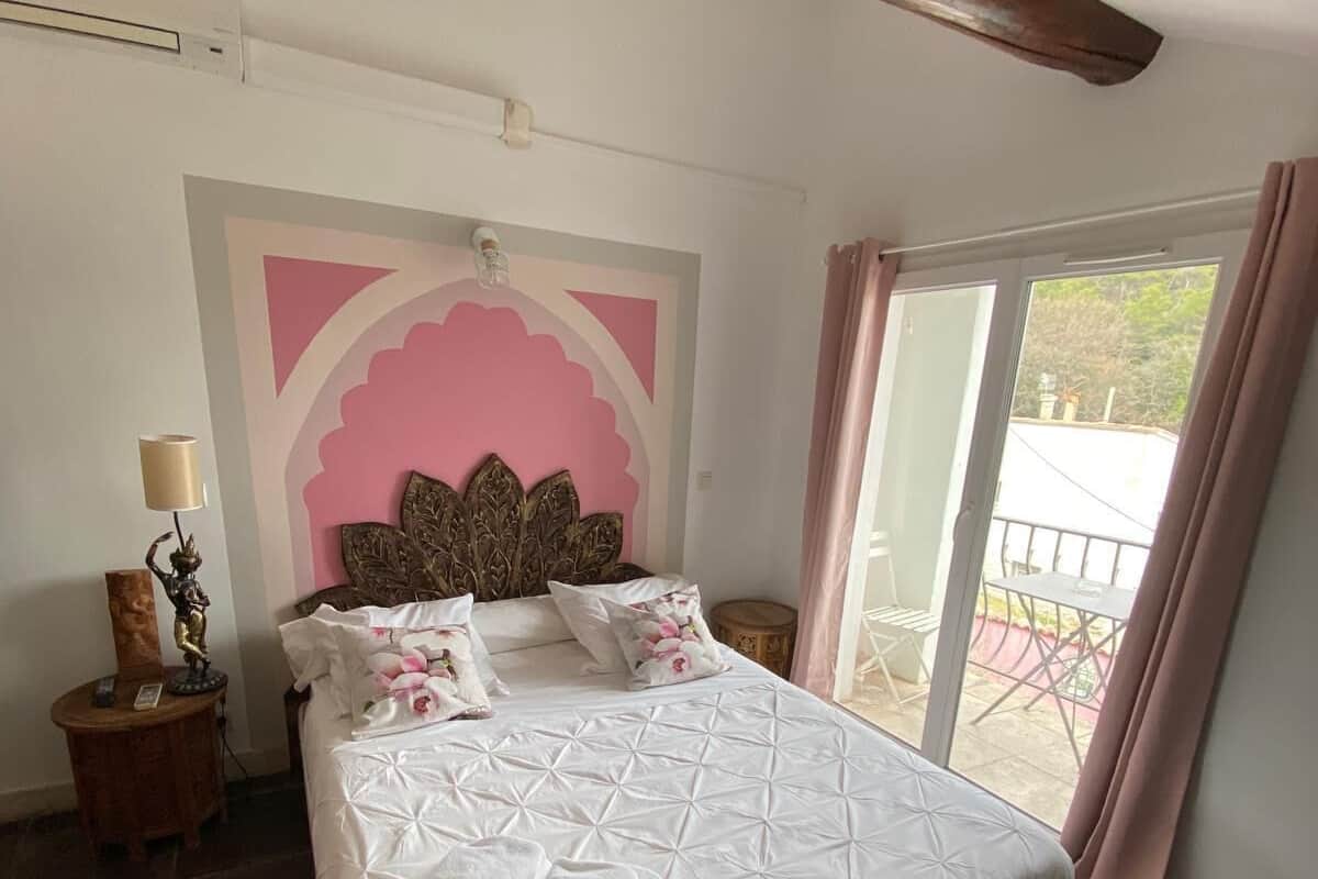 A bedroom with a large bed, a decorative headboard, a nightstand with a lamp, and a view of the outside through a sliding door.