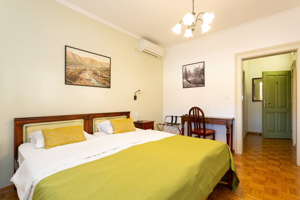 A hotel room with a bed, a desk, and two framed pictures on the wall.