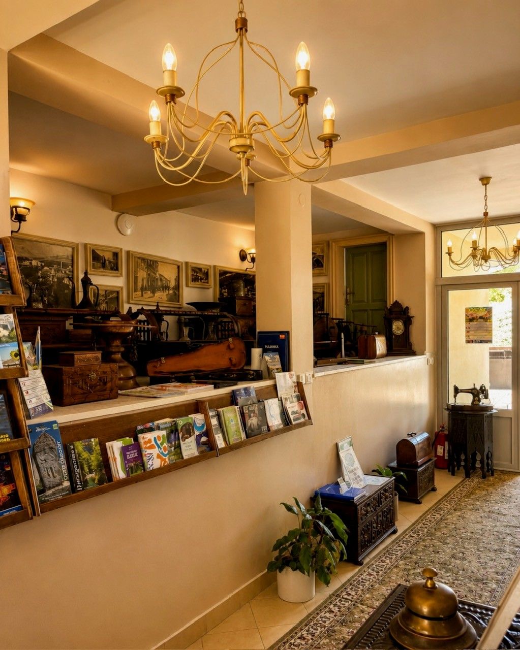 Um hall de entrada com um candelabro, uma mesa de recepção com quadros, um relógio e um tapete estampado.