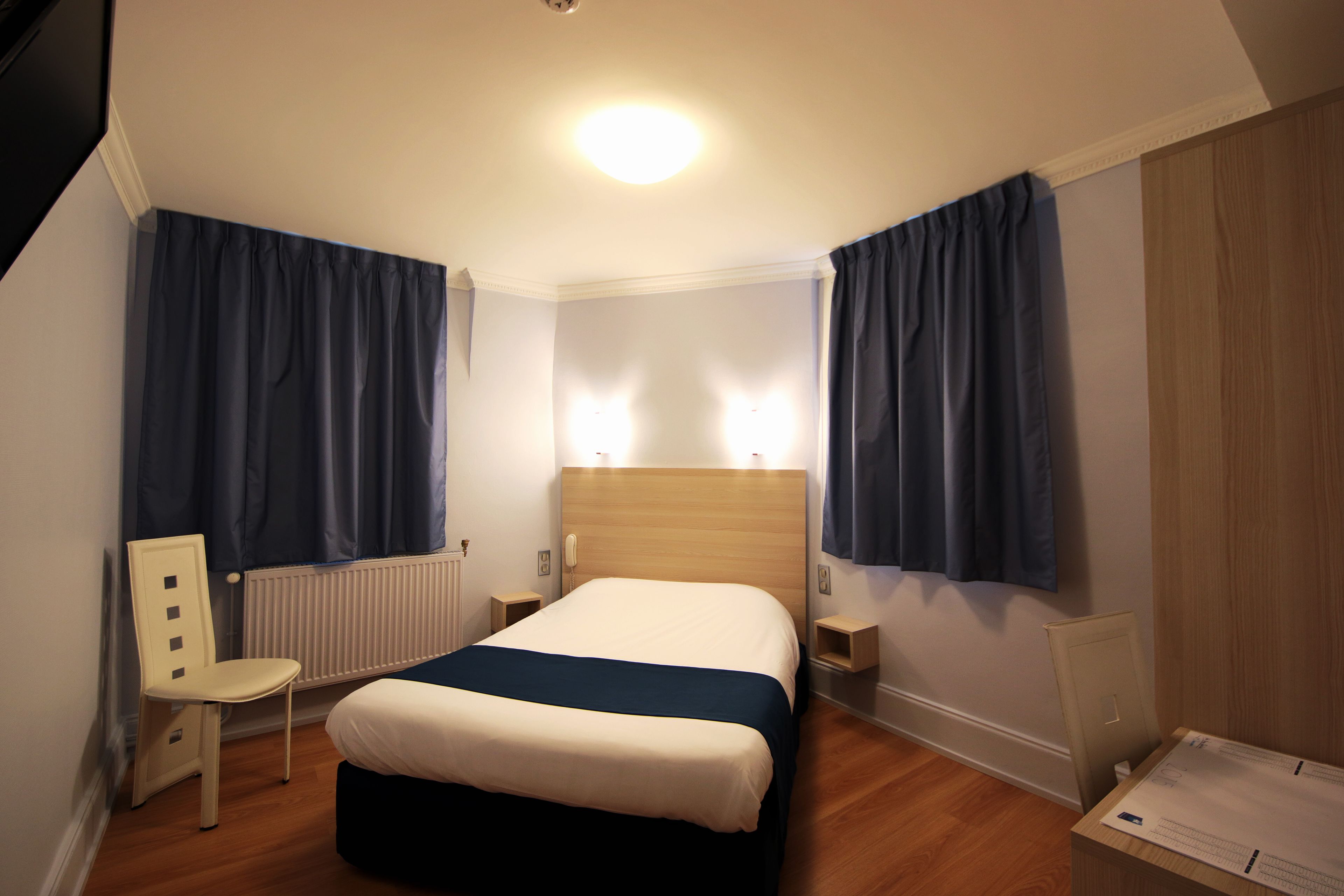 Una habitación de hotel con una cama, una silla, una mesita de noche y un atril.