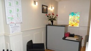 A reception area with a desk, chairs, a vase of flowers, a framed picture, and a window with a stained glass view. - Hôtel de la Cathédrale (Reims)