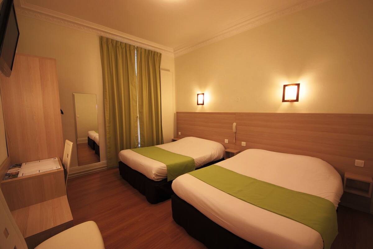 A hotel room with two beds, a desk, a chair, a mirror, and a window with curtains.
