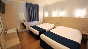 A hotel room with two beds, a wooden dresser, a mirror, and bedside lamps. - Hôtel de la Cathédrale (Reims)