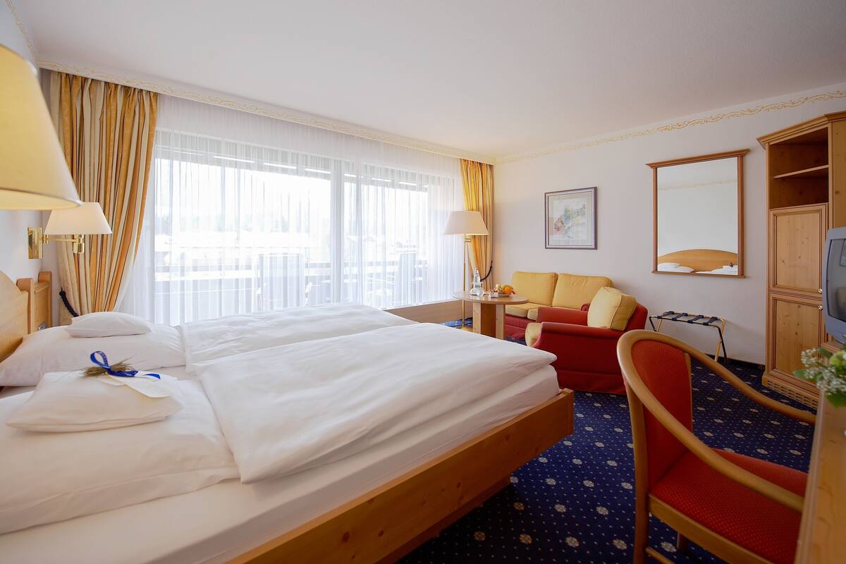 Ein Hotelzimmer mit zwei Betten, einer Couch, einem Fernseher und einem Holzschrank.