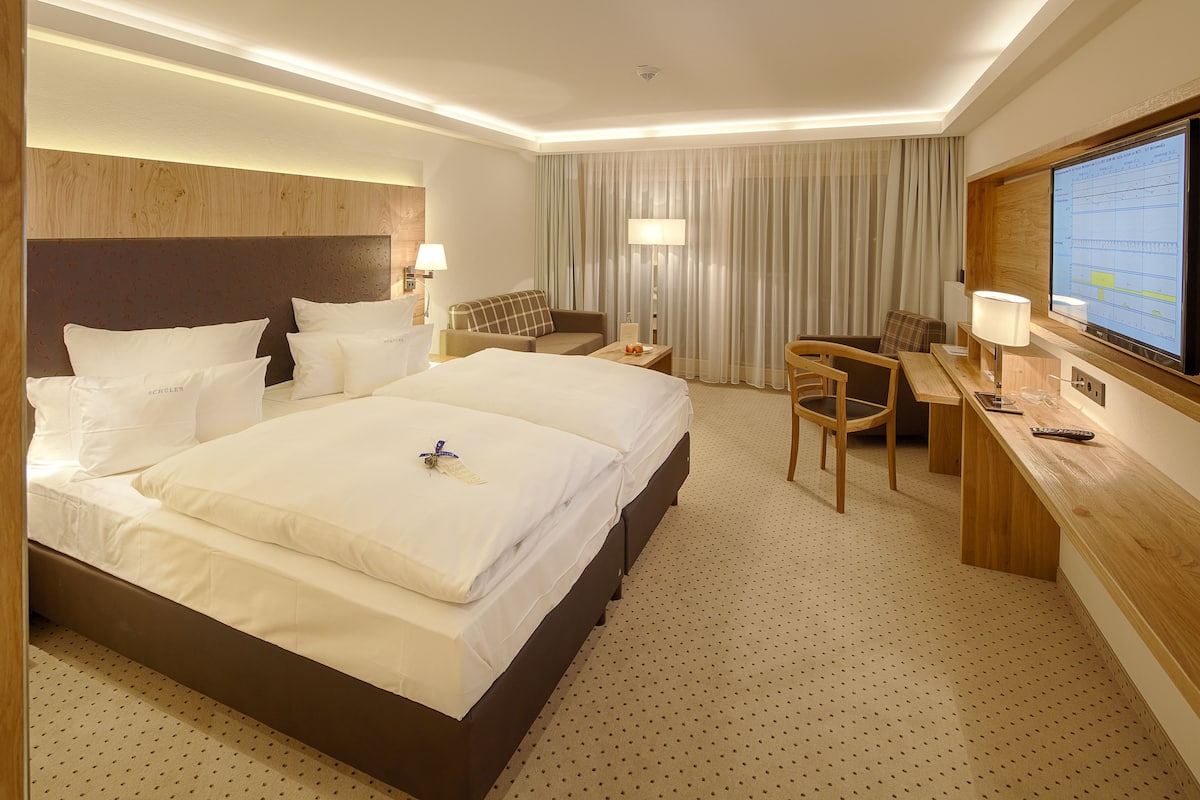 Ein Hotelzimmer mit einem großen Bett, einem Schreibtisch mit Stuhl, einem Fernseher und einem Fenster mit Vorhängen.