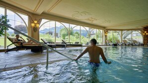An indoor swimming pool with lounge chairs and a view of the outdoors. - Schüle's Gesundheitsresort & Spa - Erwachsenenhotel (Oberstdorf)